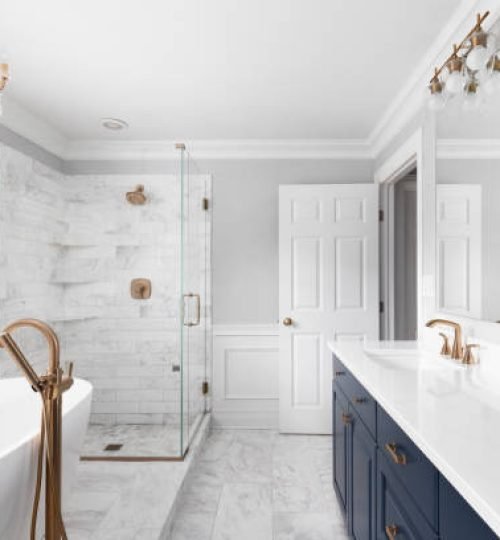 A beautiful bathroom with a blue vanity cabinet, standalone bathtub and shower, and gold faucets.